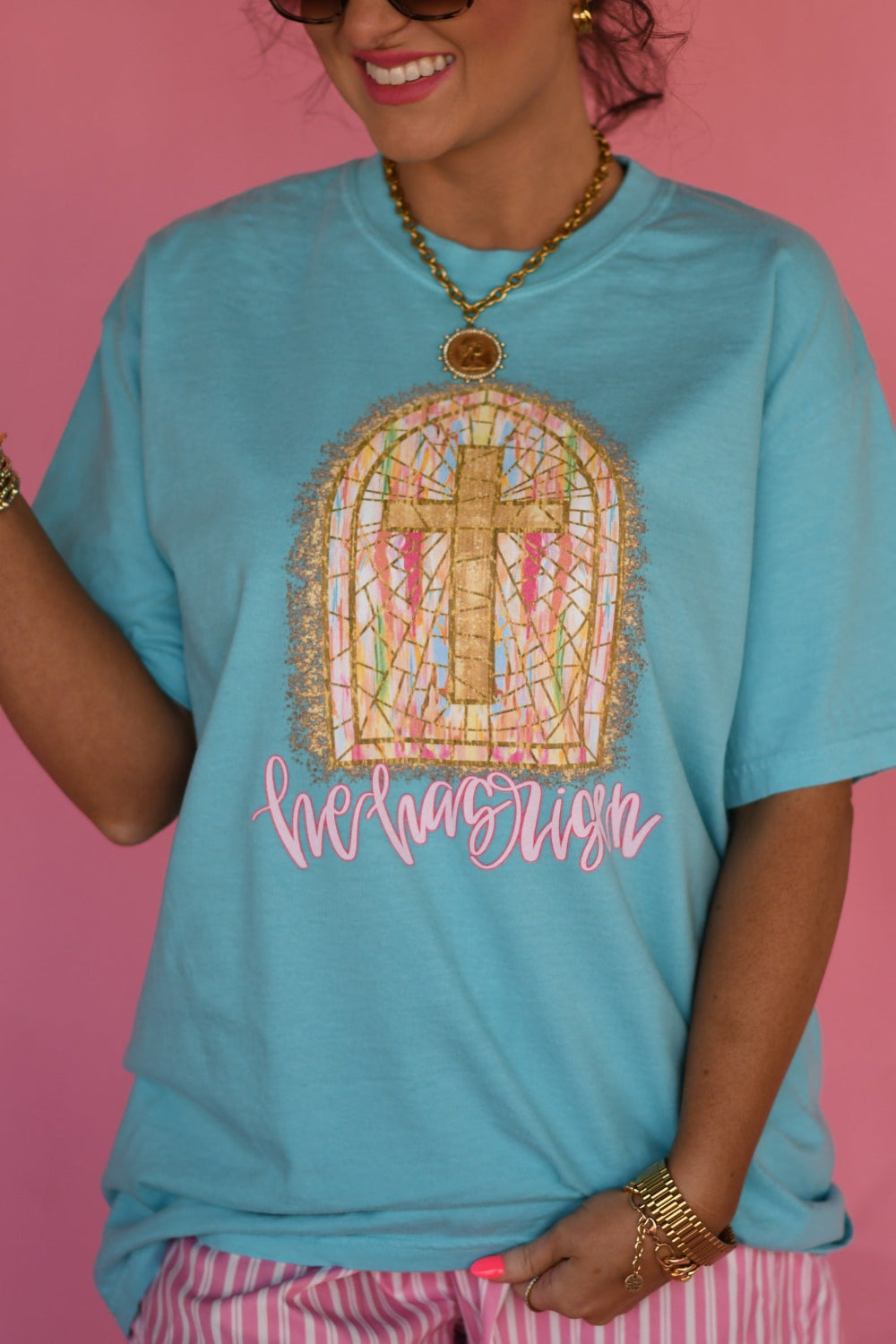 Woman modeling Lagoon Comfort Colors βHe Has Risenβ Christian Easter graphic tee featuring stained glass cross window design