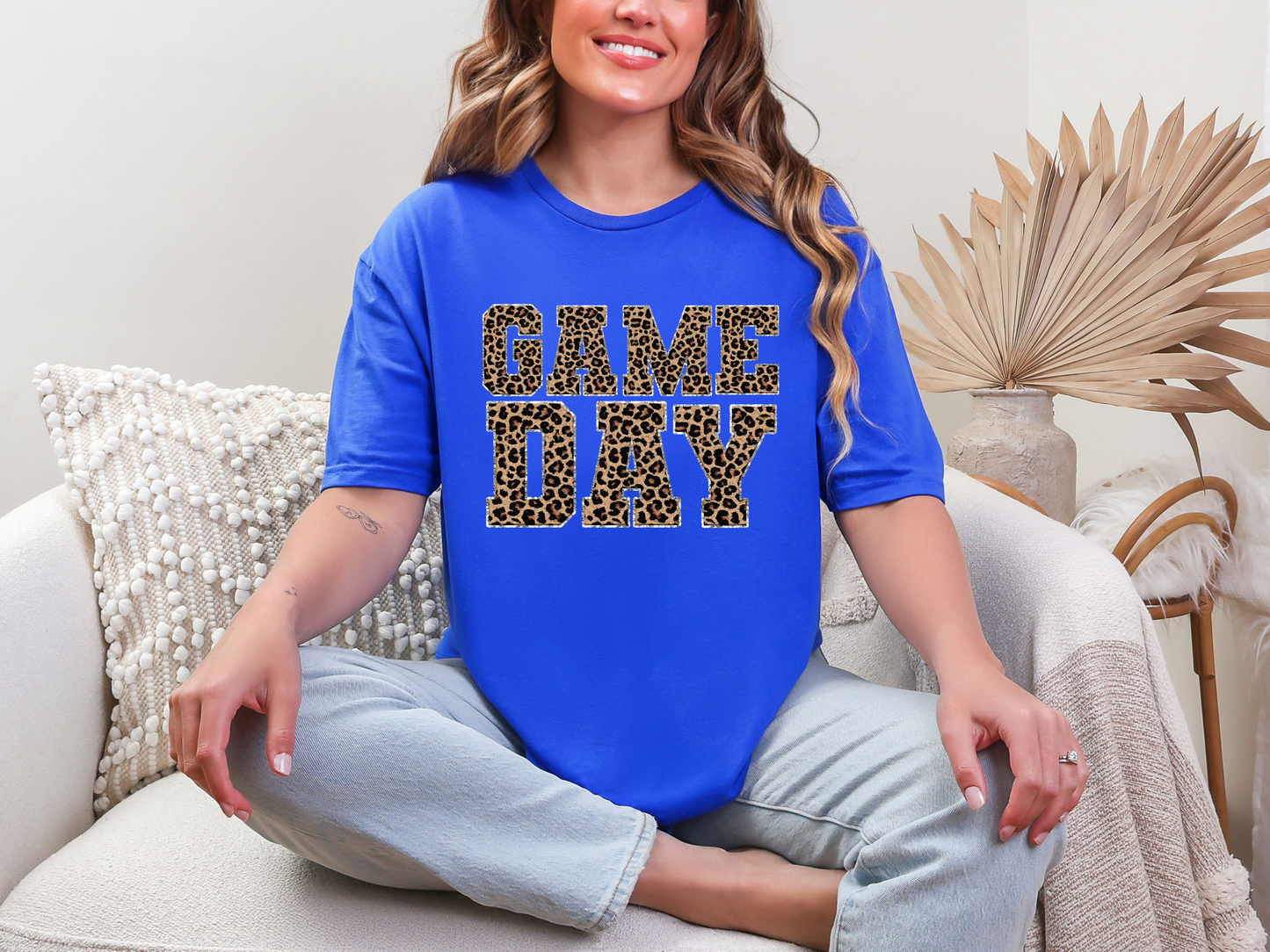Woman wearing a blue t-shirt with 'GAME DAY' in leopard print, sitting on a couch.