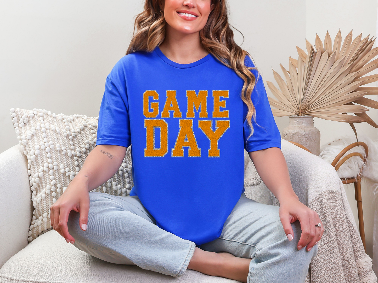 Woman wearing a blue 'GAME DAY' t-shirt sitting on a couch.