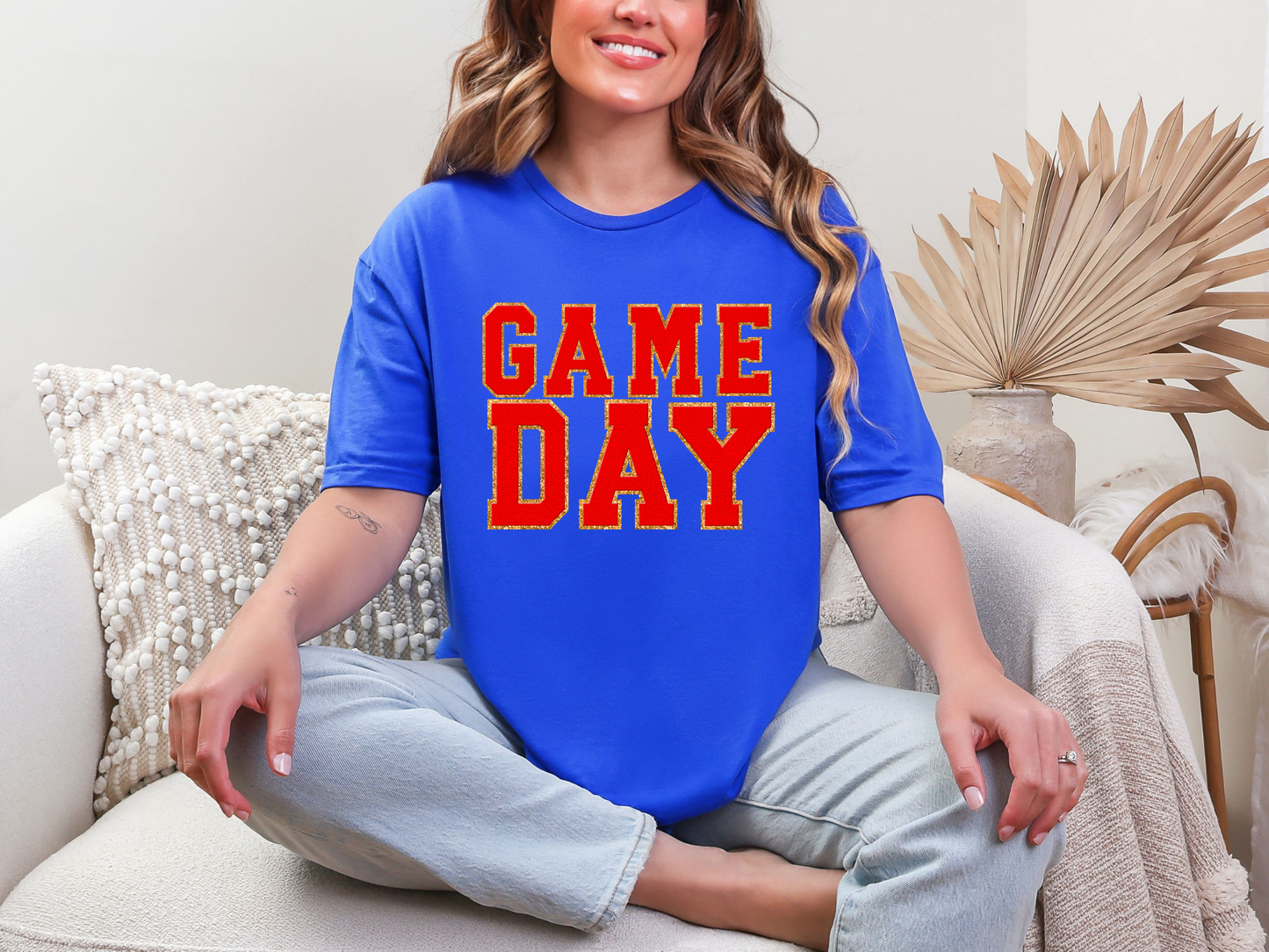 Woman wearing a blue t-shirt with 'GAME DAY' in red text, sitting on a couch.