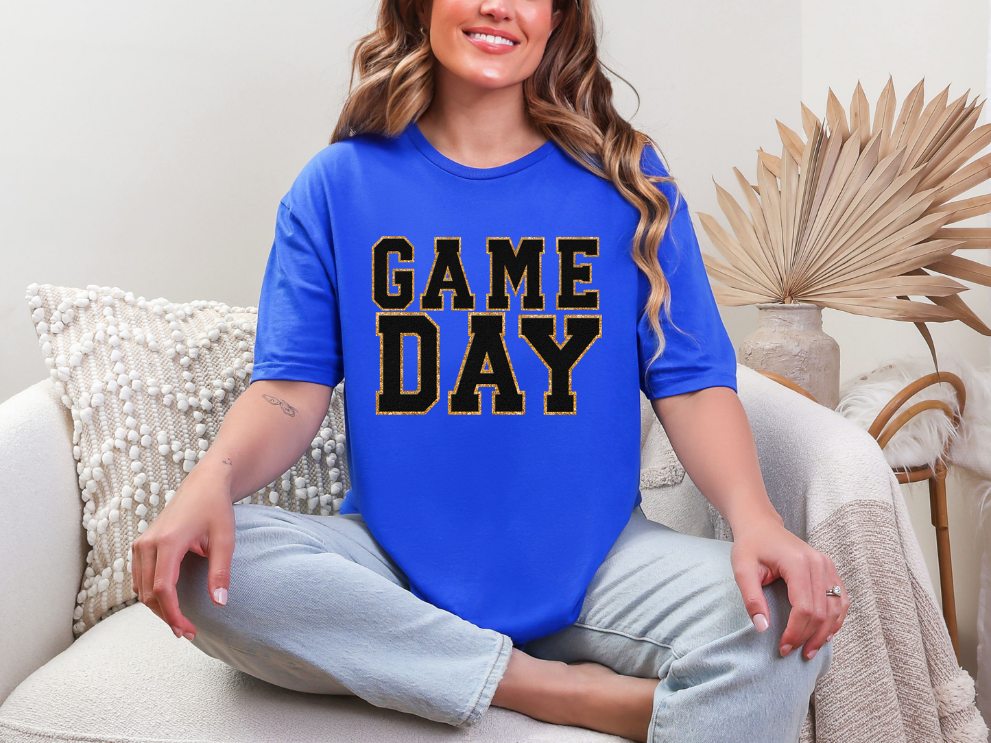 Woman wearing a blue 'GAME DAY' t-shirt sitting on a couch.