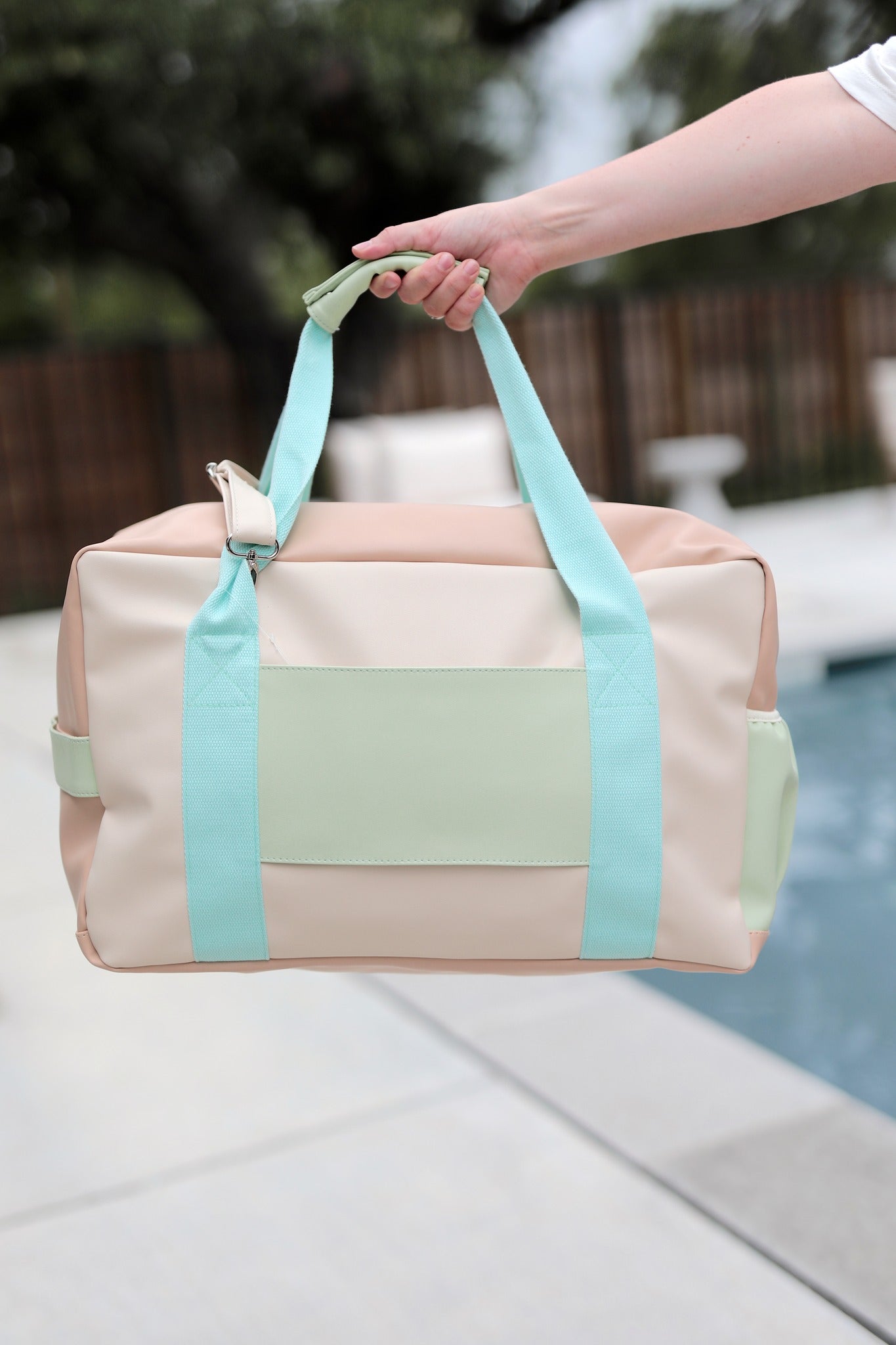 Beige and light blue duffel bag held by a hand with a blurred outdoor background