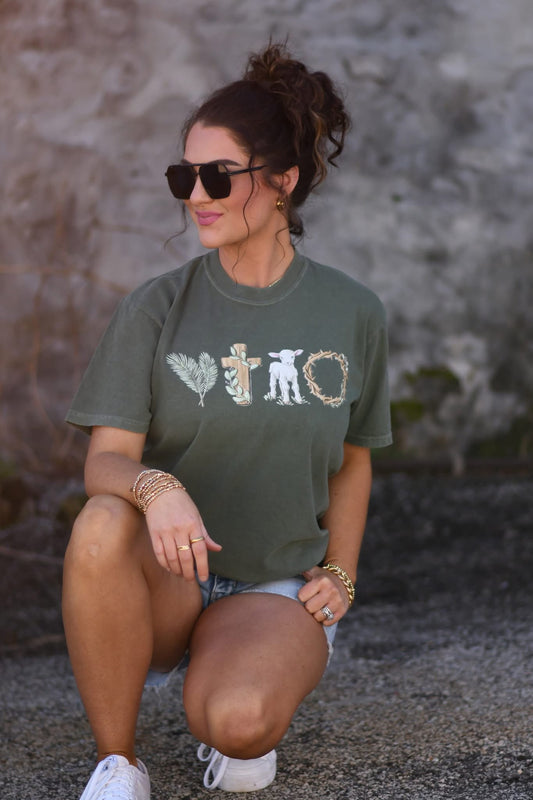 Christian Easter graphic tee in moss green featuring symbolic artwork representing the true meaning of Easter, worn with denim shorts