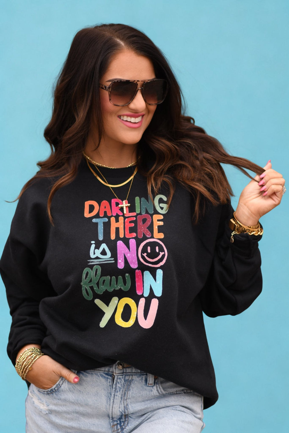 Woman wearing black sweatshirt with colorful text that reads Darling There Is No Flaw In You, positive affirmation graphic sweatshirt