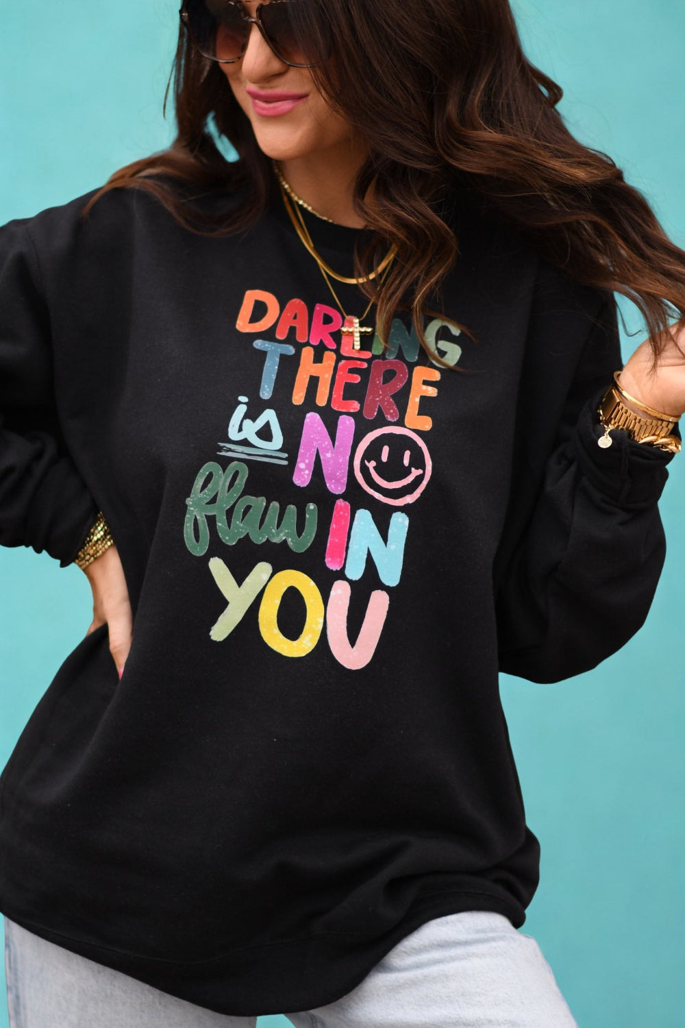 Woman wearing black sweatshirt with colorful text that reads Darling There Is No Flaw In You, positive affirmation graphic sweatshirt