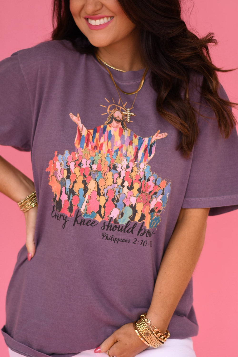 Woman wearing a wine colored Comfort Colors Christian graphic t-shirt featuring Jesus with raised arms above a colorful crowd and the phrase “Every Knee Should Bow” on a pink background