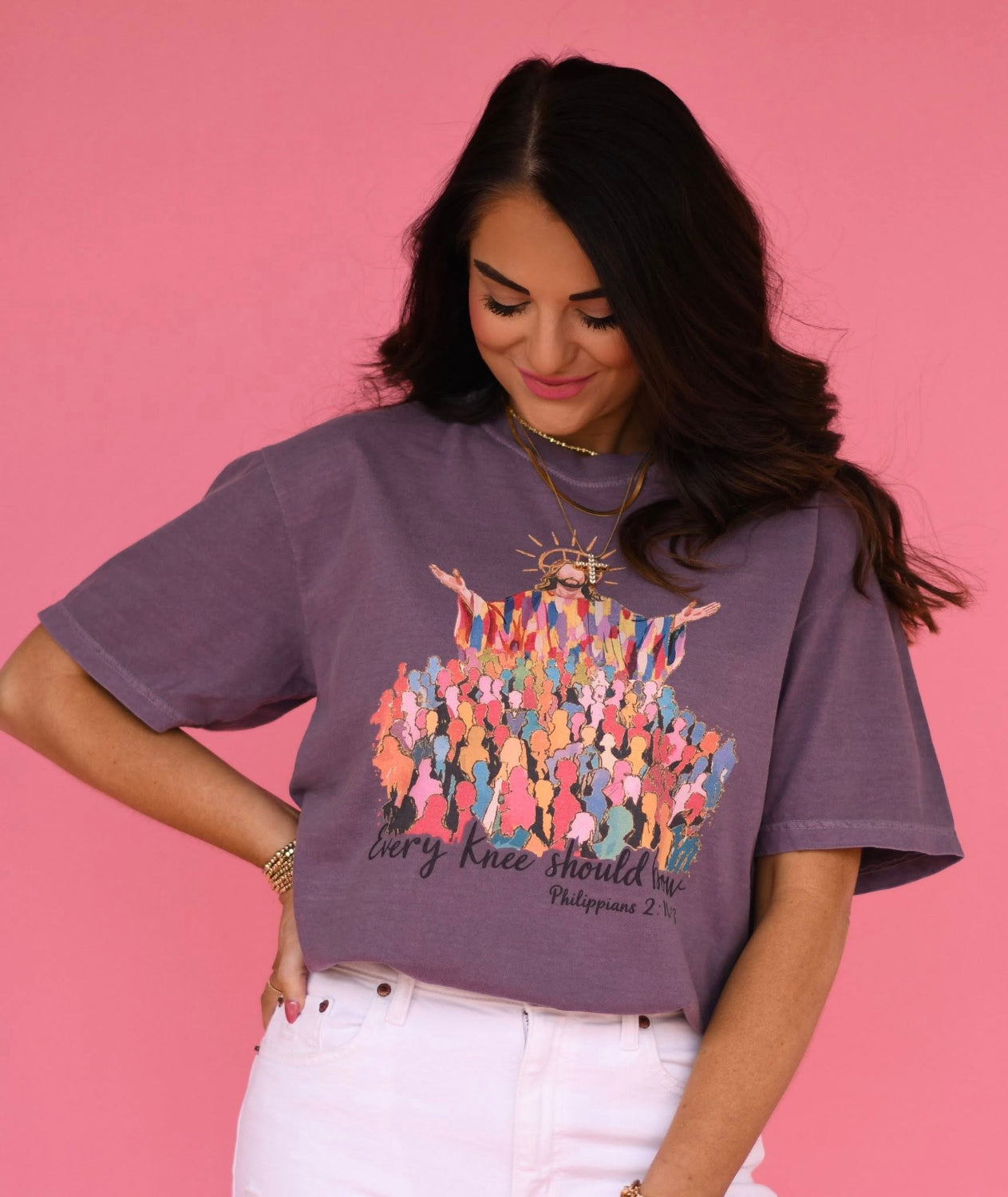 Woman wearing a wine colored Comfort Colors Christian graphic t-shirt featuring Jesus with raised arms above a colorful crowd and the phrase “Every Knee Should Bow” on a pink background
