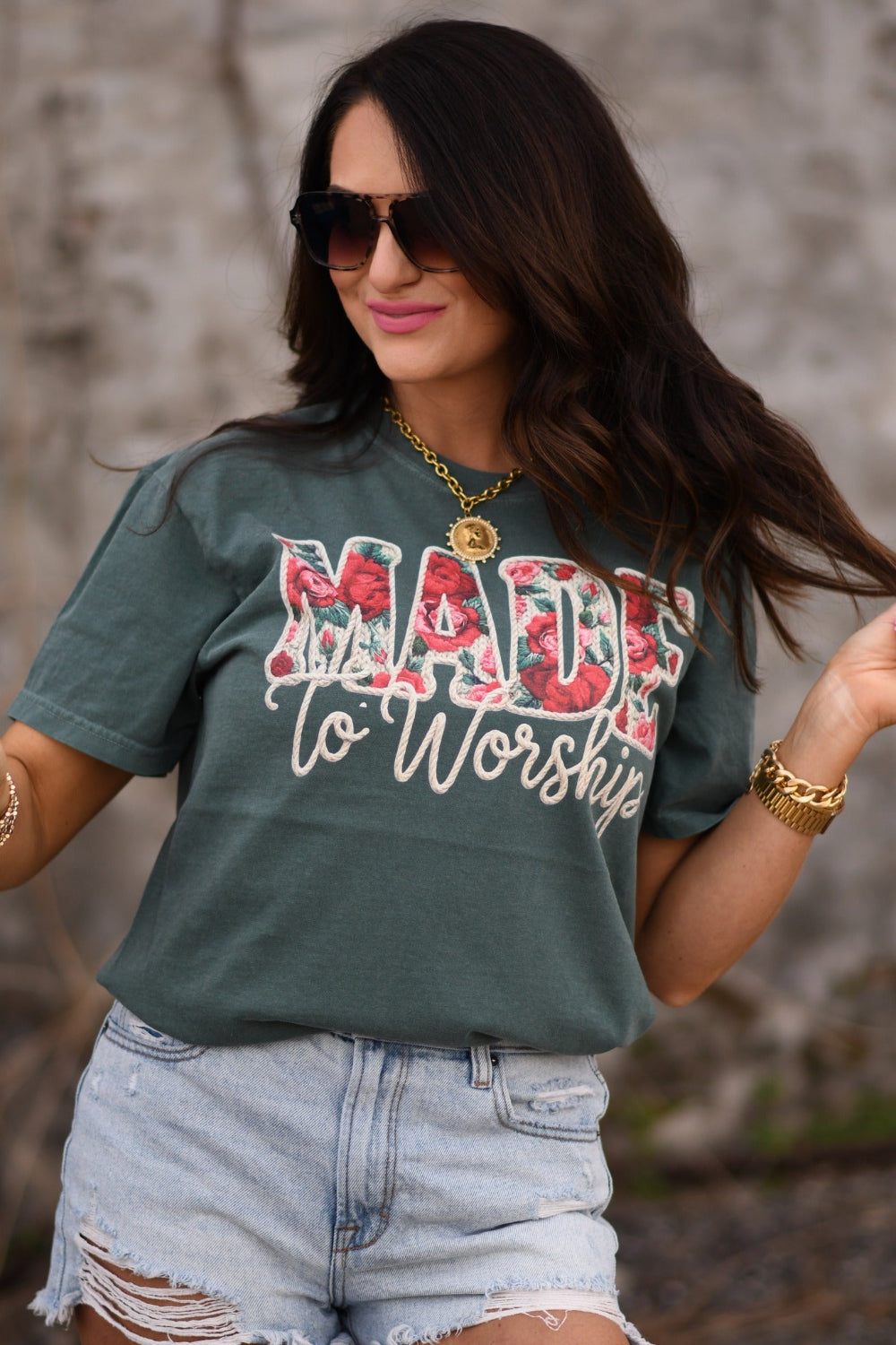 Woman wearing Blue Spruce Comfort Colors Made To Worship floral Christian graphic tee styled with distressed denim shorts and gold accessories.