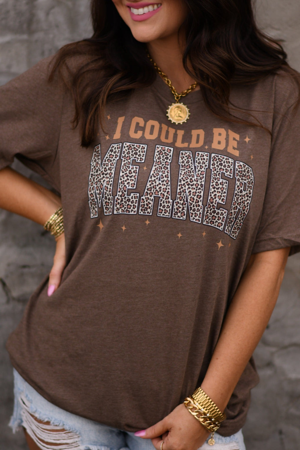 Woman wearing heather brown I Could Be Meaner leopard graphic tee on Bella Canvas unisex t-shirt with distressed denim shorts and gold jewelry