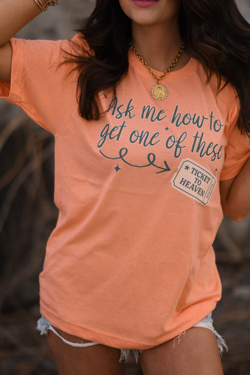 Woman wearing a heather cantaloupe Christian graphic tee that says “Ask Me How To Get One Of These” with Ticket to Heaven design, Tultex unisex fit faith shirt