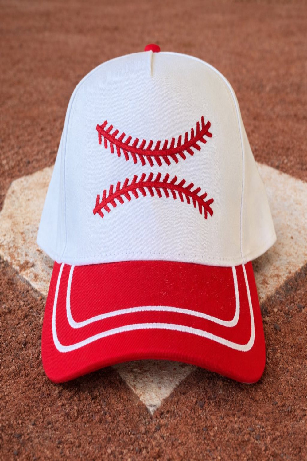Four embroidered baseball-themed two-tone snapback hats in red, blue, orange, and black displayed on a baseball field.