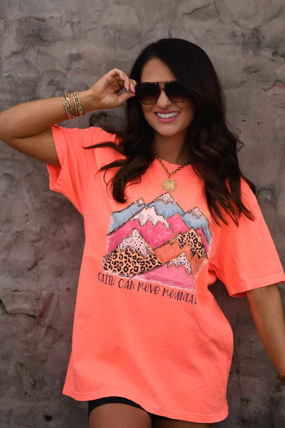 Woman wearing neon red orange Faith Can Move Mountains graphic tee with colorful mountain and leopard print design printed on Comfort Colors unisex fit shirt