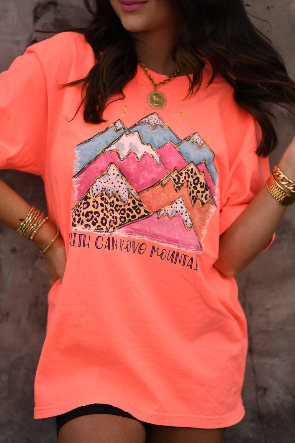 Woman wearing neon red orange Faith Can Move Mountains graphic tee with colorful mountain and leopard print design printed on Comfort Colors unisex fit shirt