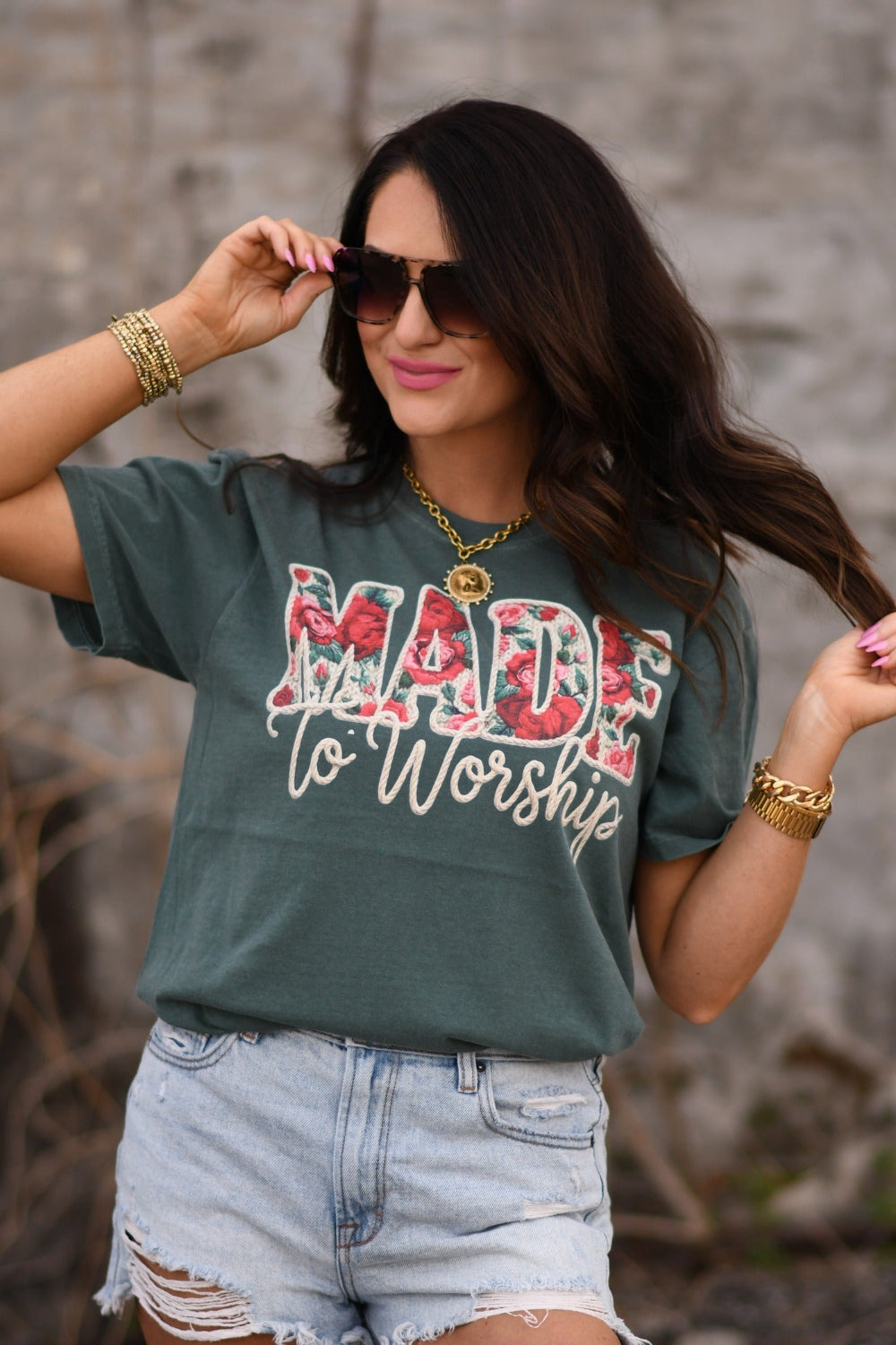 Woman wearing Blue Spruce Comfort Colors Made To Worship floral Christian graphic tee styled with distressed denim shorts and gold accessories.