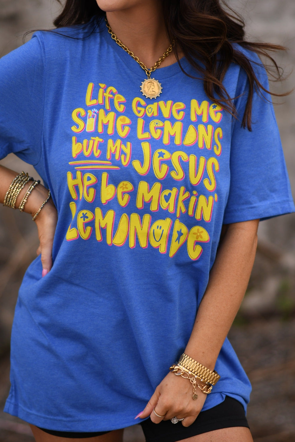 Woman wearing a Heather Royal Blue Bella Canvas unisex graphic tee that says "Life Gave Me Some Lemons but My Jesus He Be Makin' Lemonade" with yellow lemon design.