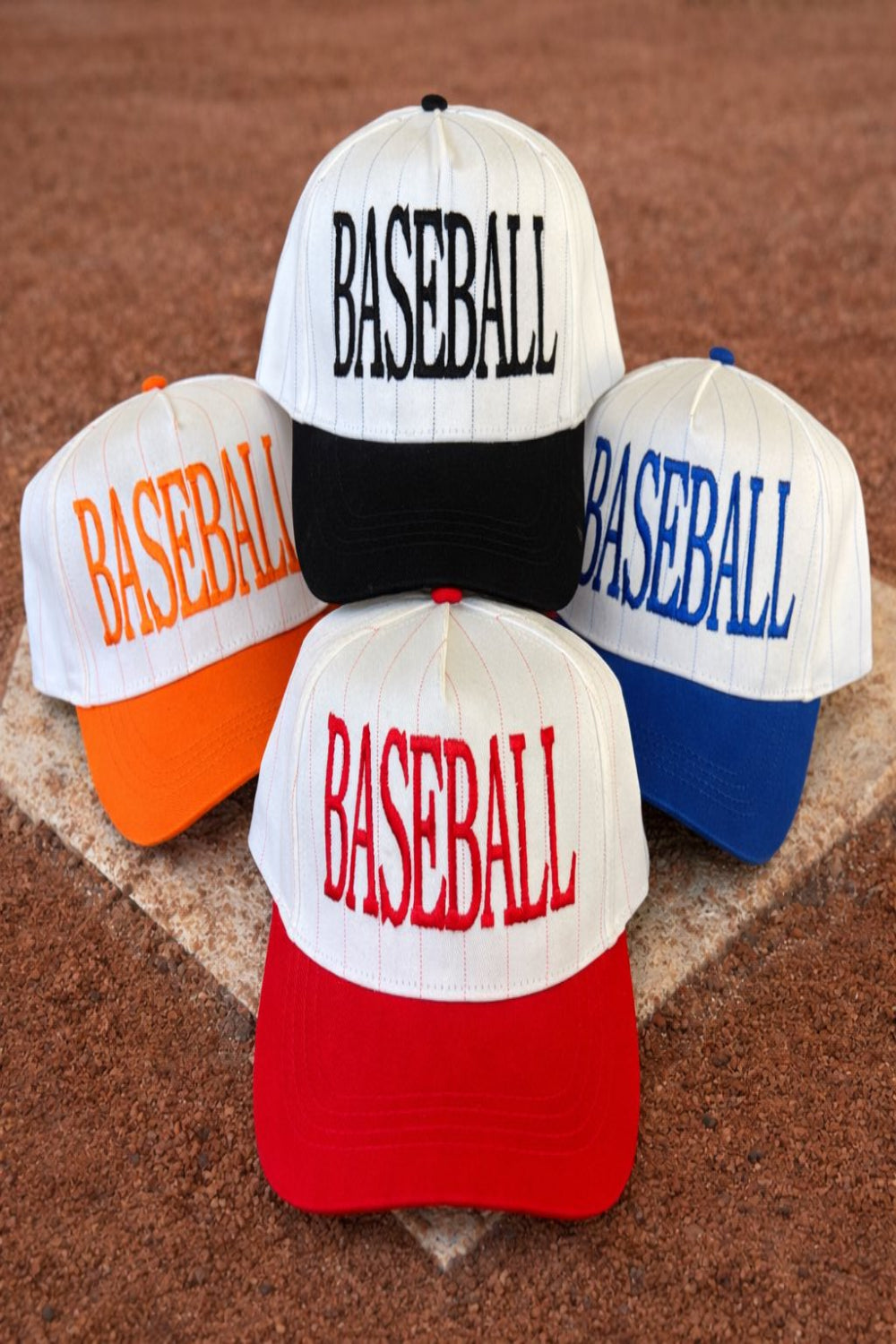 Four embroidered baseball-themed two-tone snapback hats in red, blue, orange, and black displayed on a baseball field.