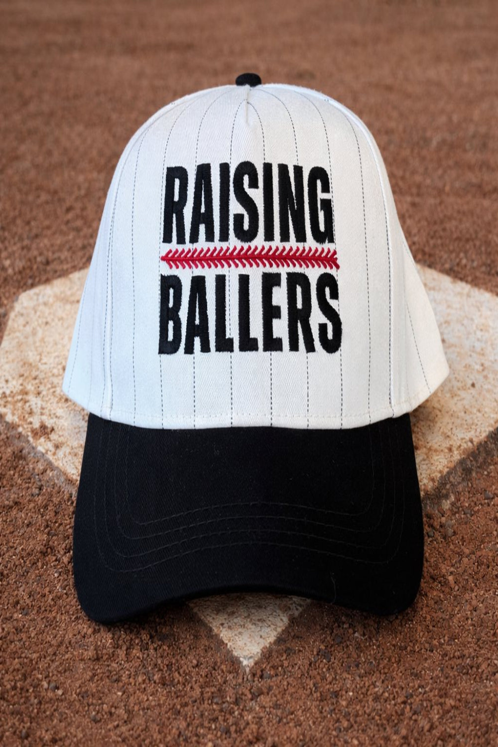 Baseball cap with 'RAISING BALLERS' text on a baseball field