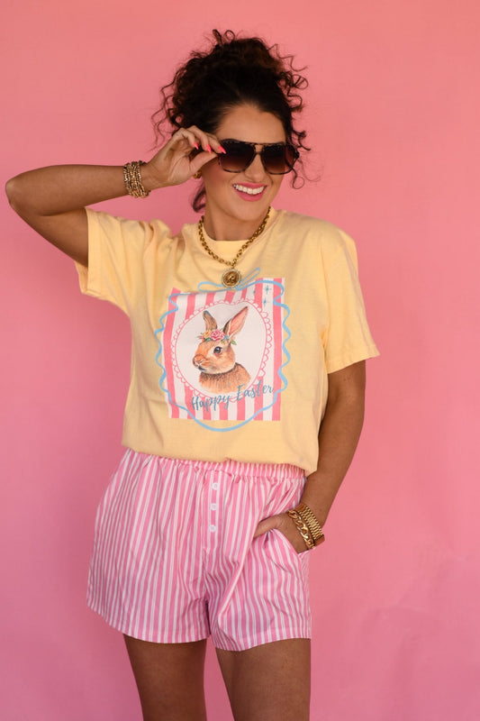 Woman wearing pastel yellow vintage bunny Easter graphic t-shirt with pink striped shorts against pink background