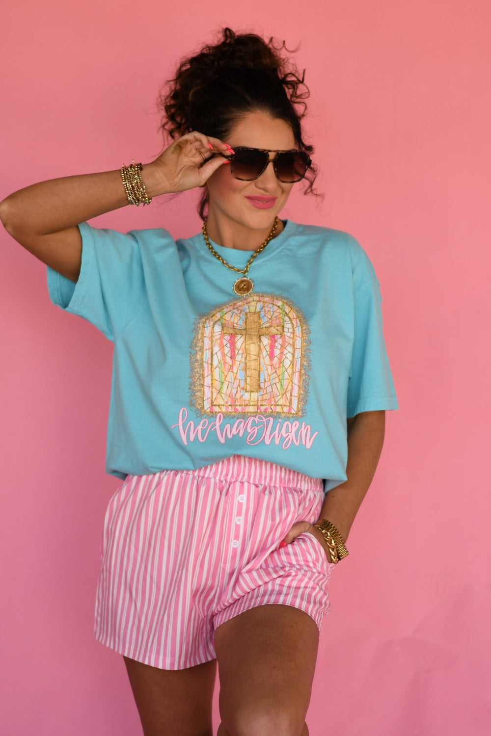 Woman modeling Lagoon Comfort Colors “He Has Risen” Christian Easter graphic tee featuring stained glass cross window design