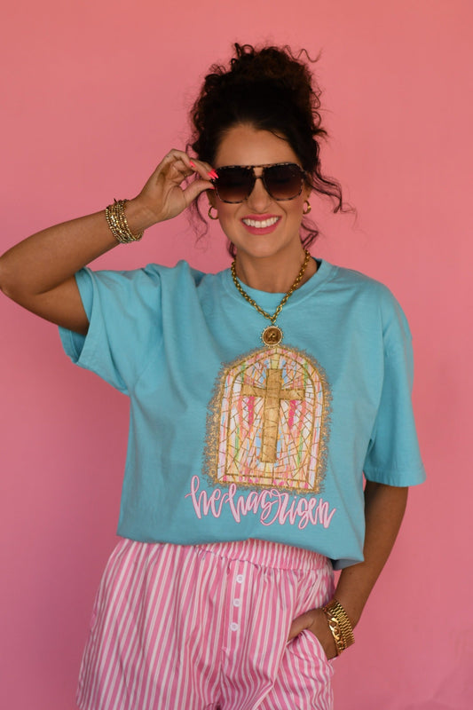 Woman modeling Lagoon Comfort Colors “He Has Risen” Christian Easter graphic tee featuring stained glass cross window design