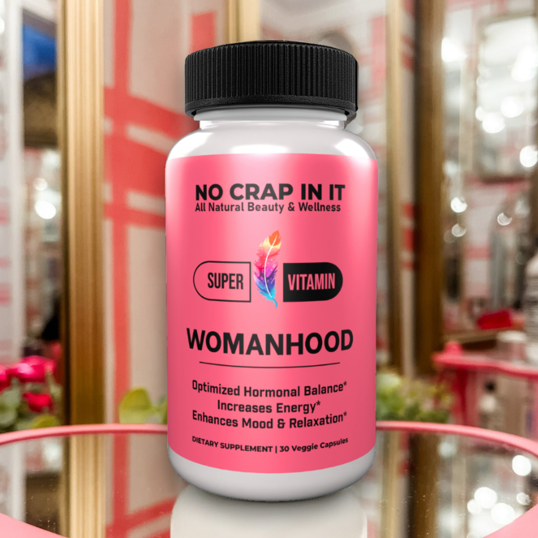 A bottle of 'No Crap In It' Womanhood Super Vitamin Supplement with pink label, black cap, and text indicating optimized hormonal balance, increased energy, and enhanced mood and relaxation.