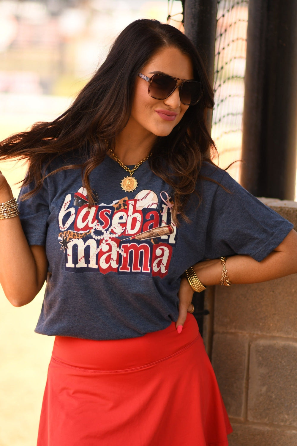 Baseball Mama Icons graphic tee in heather navy worn by woman with red athletic skirt at baseball field