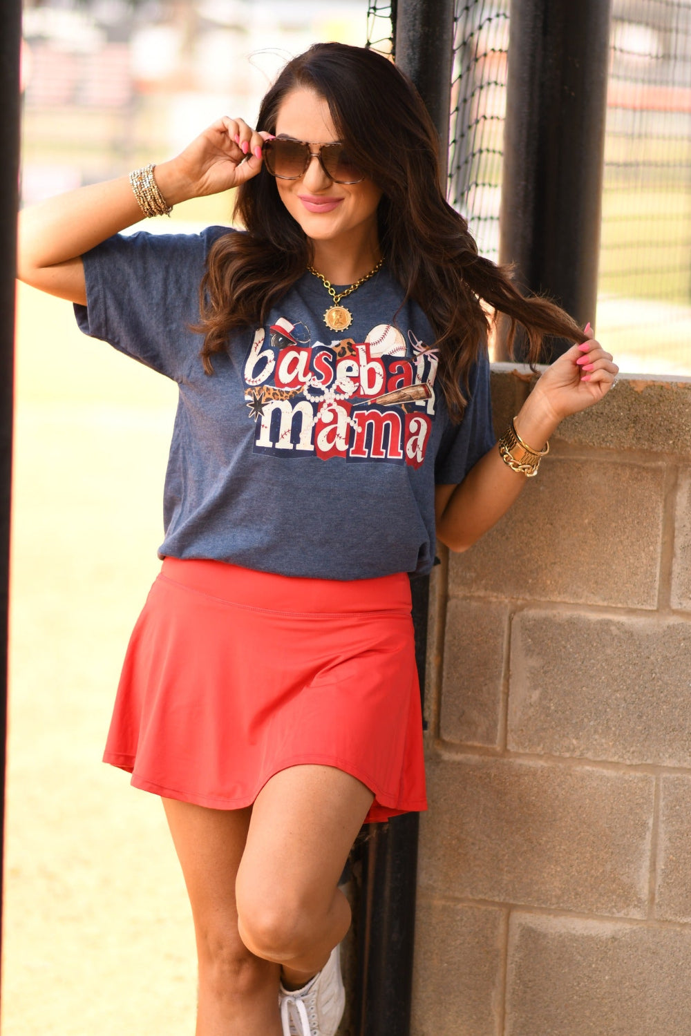 Baseball Mama Icons graphic tee in heather navy worn by woman with red athletic skirt at baseball field