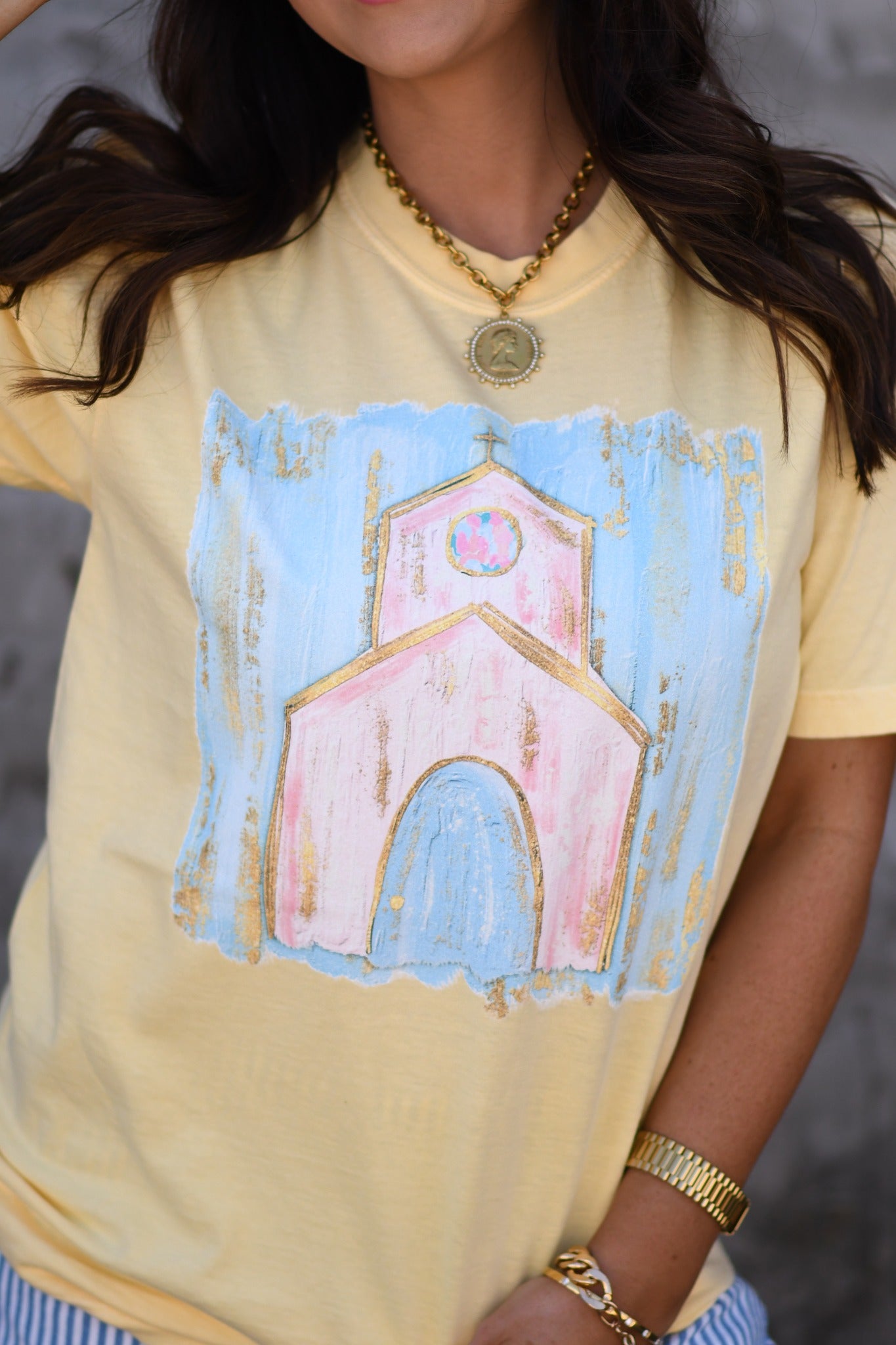 Woman wearing butter yellow church graphic tee with pastel design and pink cross embroidered snapback hat