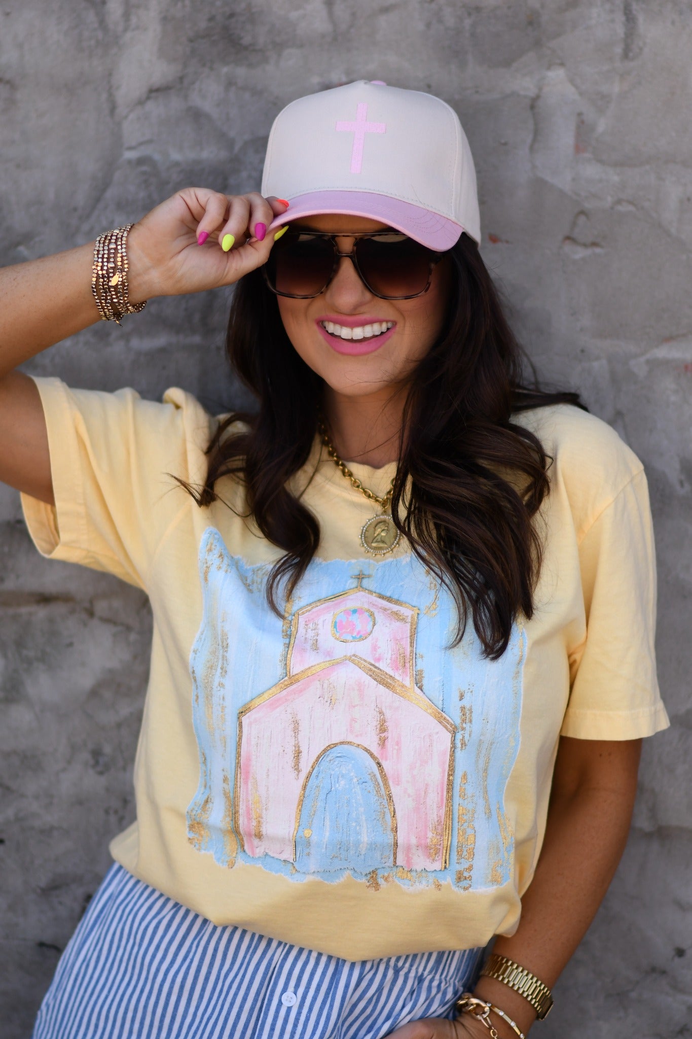 Woman wearing butter yellow church graphic tee with pastel design and pink cross embroidered snapback hat