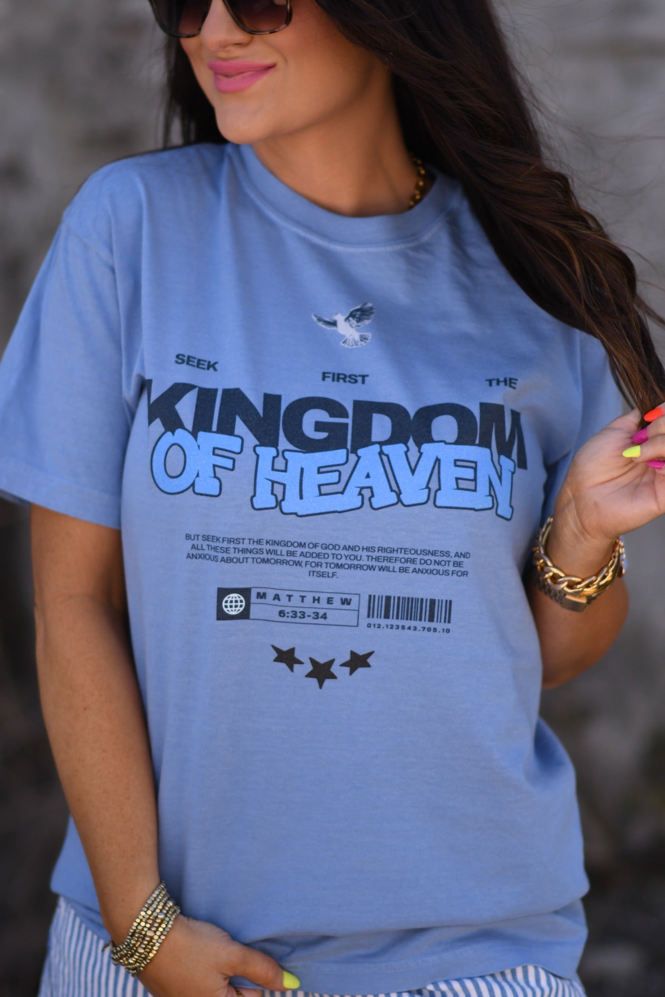 Woman wearing a washed denim Kingdom of Heaven receipt graphic t-shirt with sunglasses and gold jewelry