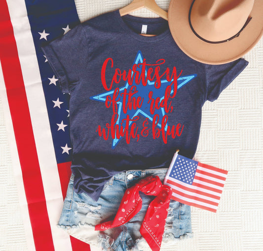 Courtesy of the Red White and Blue patriotic graphic tee on a navy Tultex unisex shirt styled with denim shorts, American flag, red bandana, and tan hat.