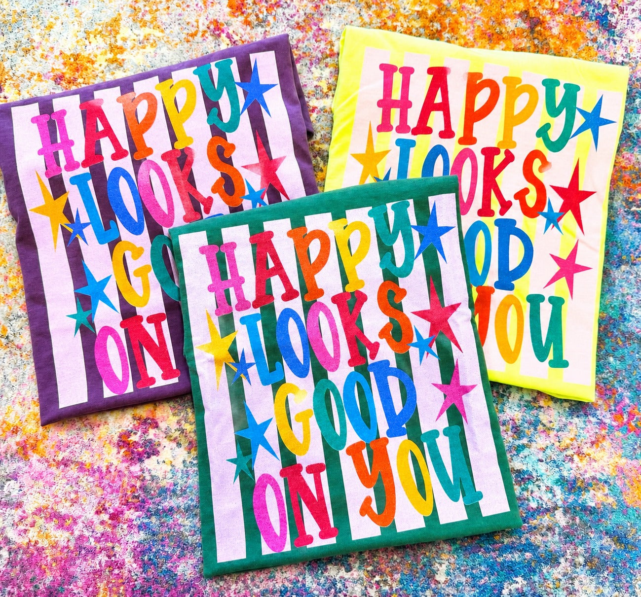 Colorful Happy Looks Good On You graphic tees on Comfort Colors shirts in neon lemon, light green, and berry with bright retro lettering and star details.