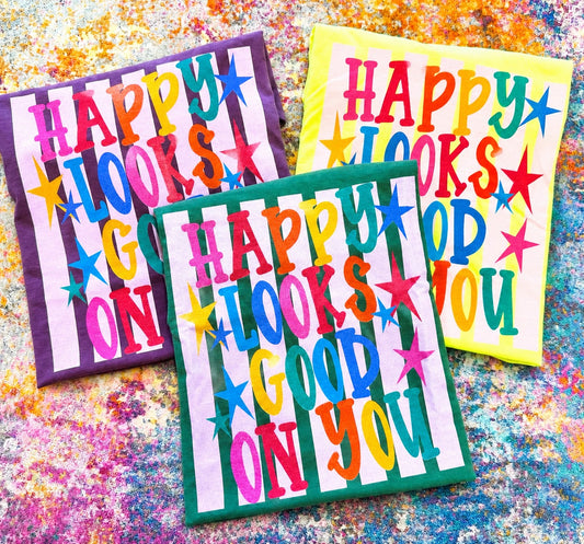 Colorful Happy Looks Good On You graphic tees on Comfort Colors shirts in neon lemon, light green, and berry with bright retro lettering and star details.
