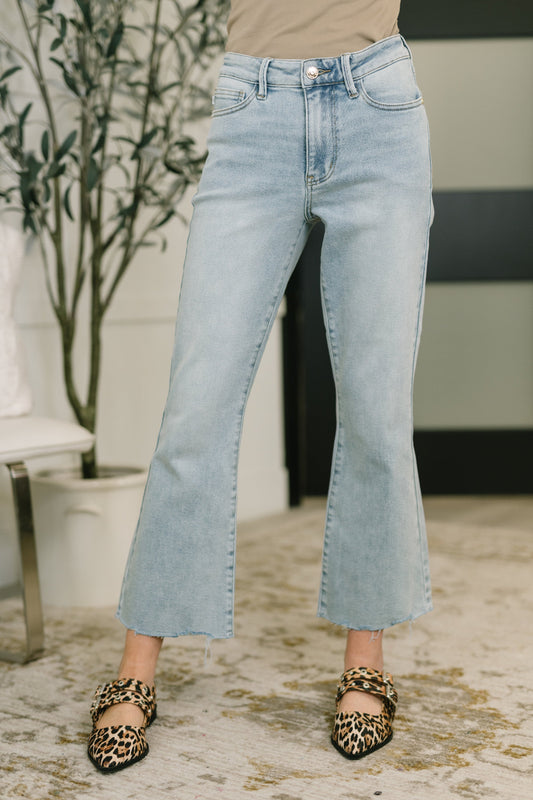 Model wearing Judy Blue mid rise kick flare jeans in light wash with raw hem, styled with a neutral tank and leopard flats
