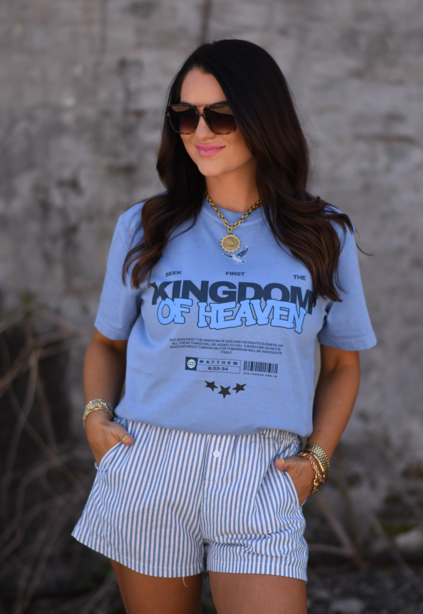 Woman wearing a washed denim Kingdom of Heaven receipt graphic t-shirt with sunglasses and gold jewelry