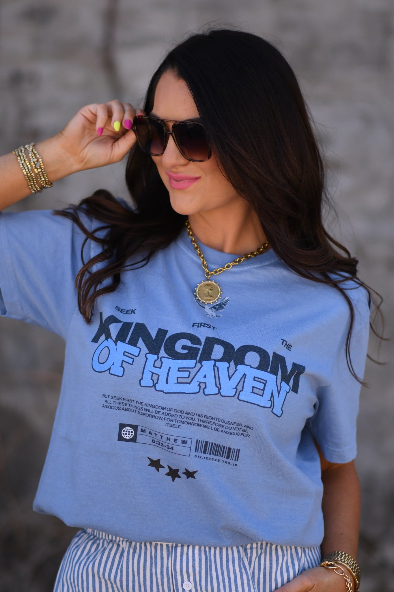Woman wearing a washed denim Kingdom of Heaven receipt graphic t-shirt with sunglasses and gold jewelry