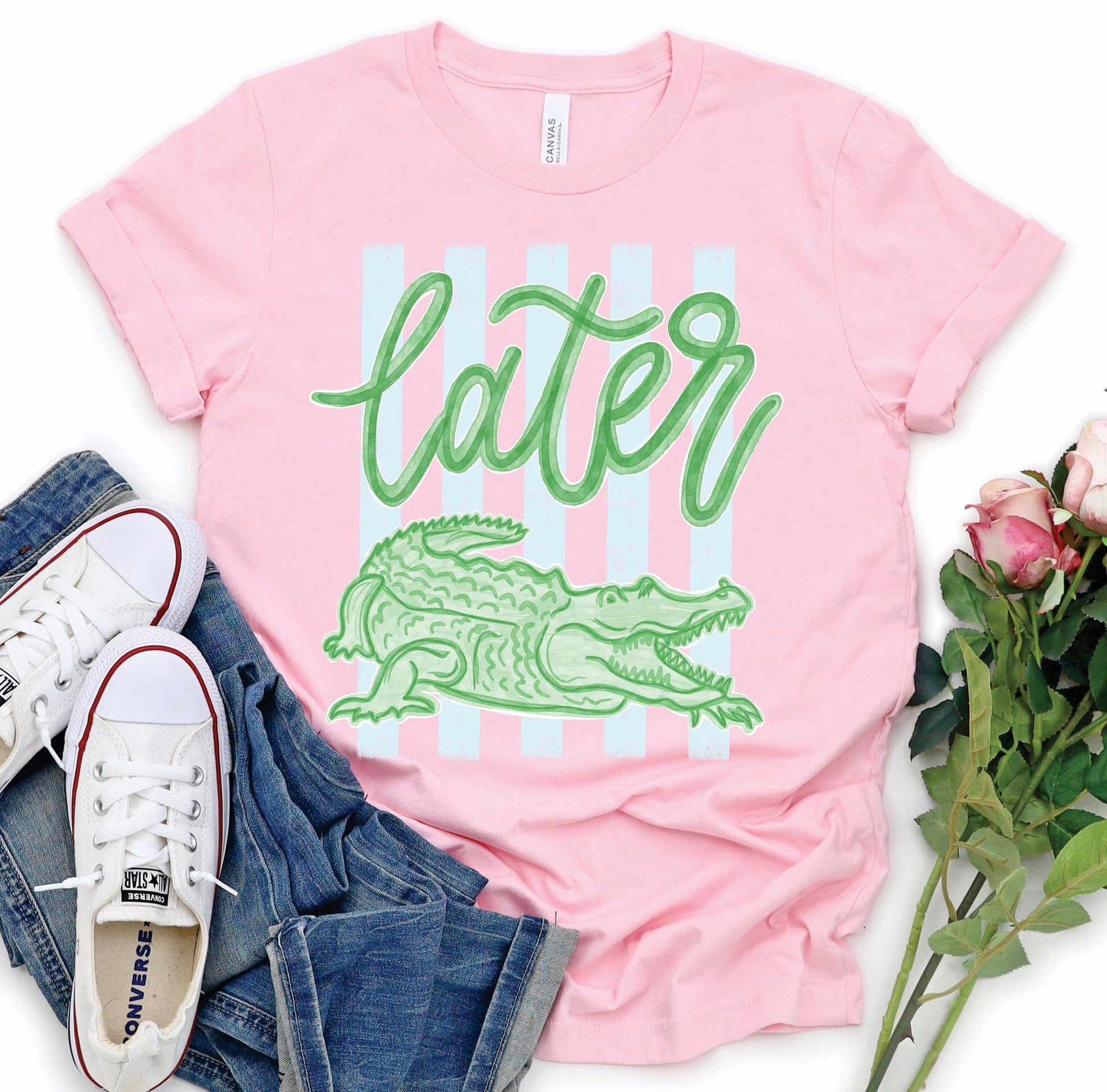 Pink Bella Canvas t-shirt with green “Later Gator” script and alligator graphic over pastel stripes, styled with jeans and white sneakers