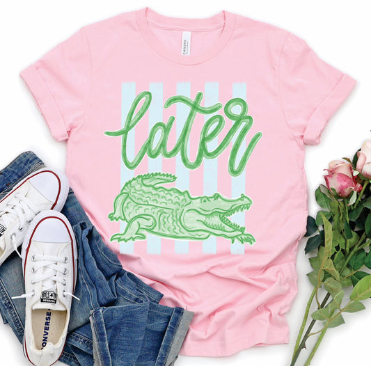 Pink Bella Canvas t-shirt with green “Later Gator” script and alligator graphic over pastel stripes, styled with jeans and white sneakers
