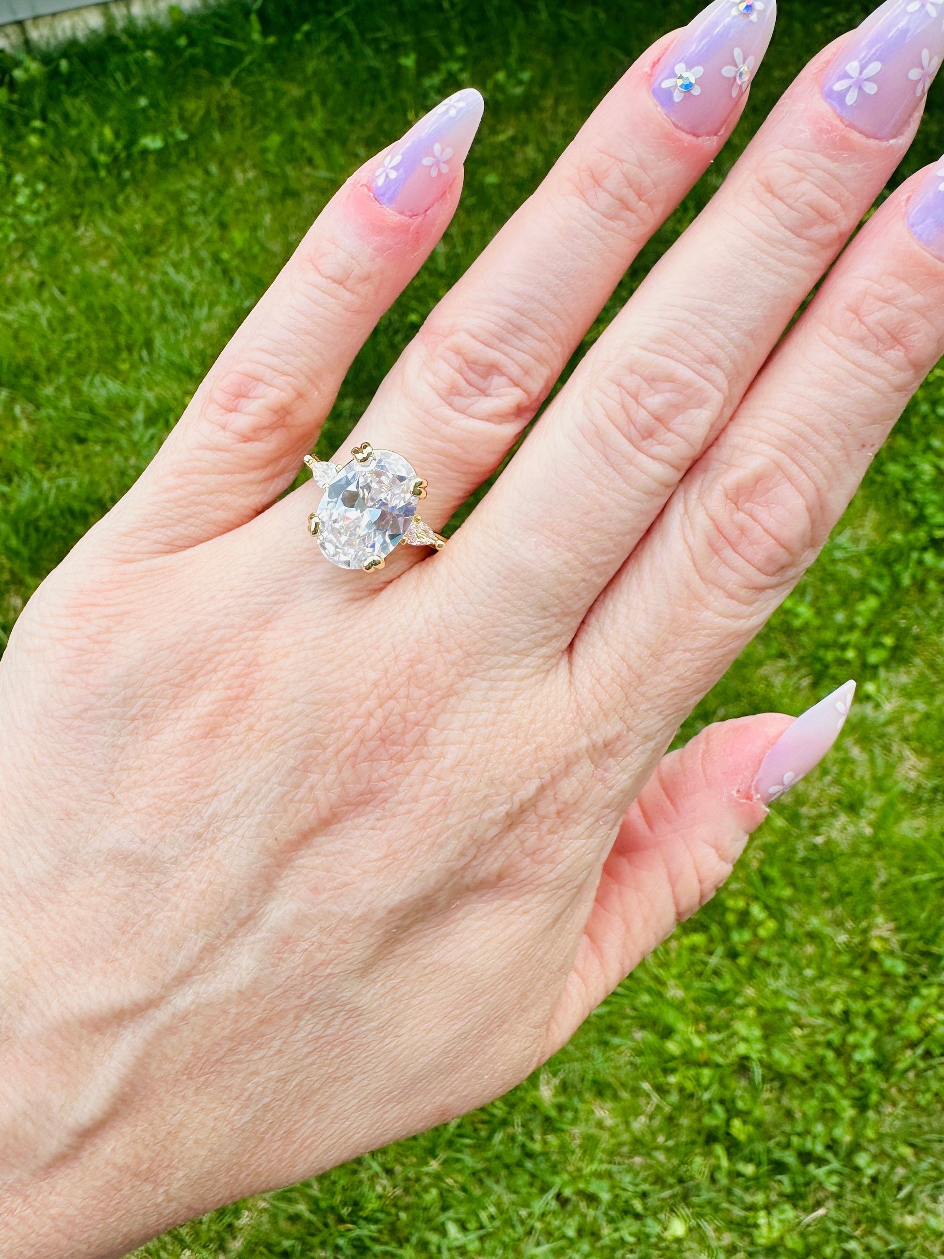 Hand wearing Liora Luxe oval three-stone gold plated ring with large cubic zirconia center stone and floral nail art