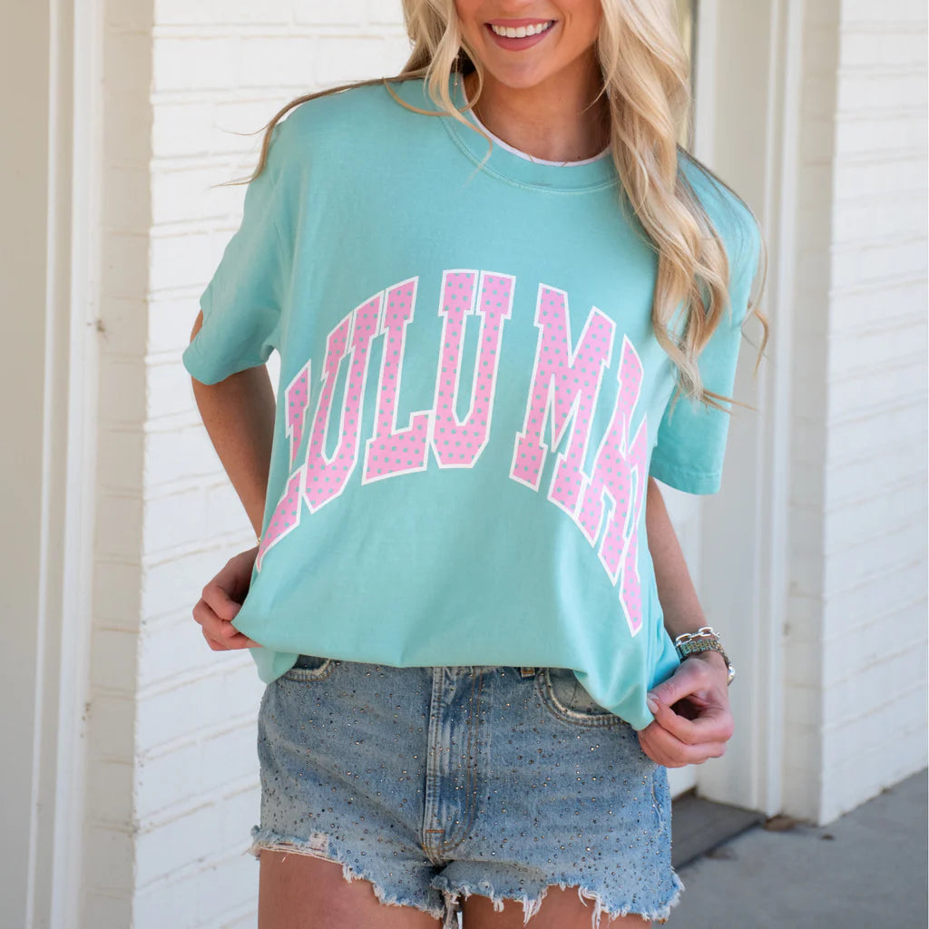 Woman wearing a chalky mint Comfort Colors t-shirt with pink polka dot Lulu Mac graphic paired with distressed denim shorts