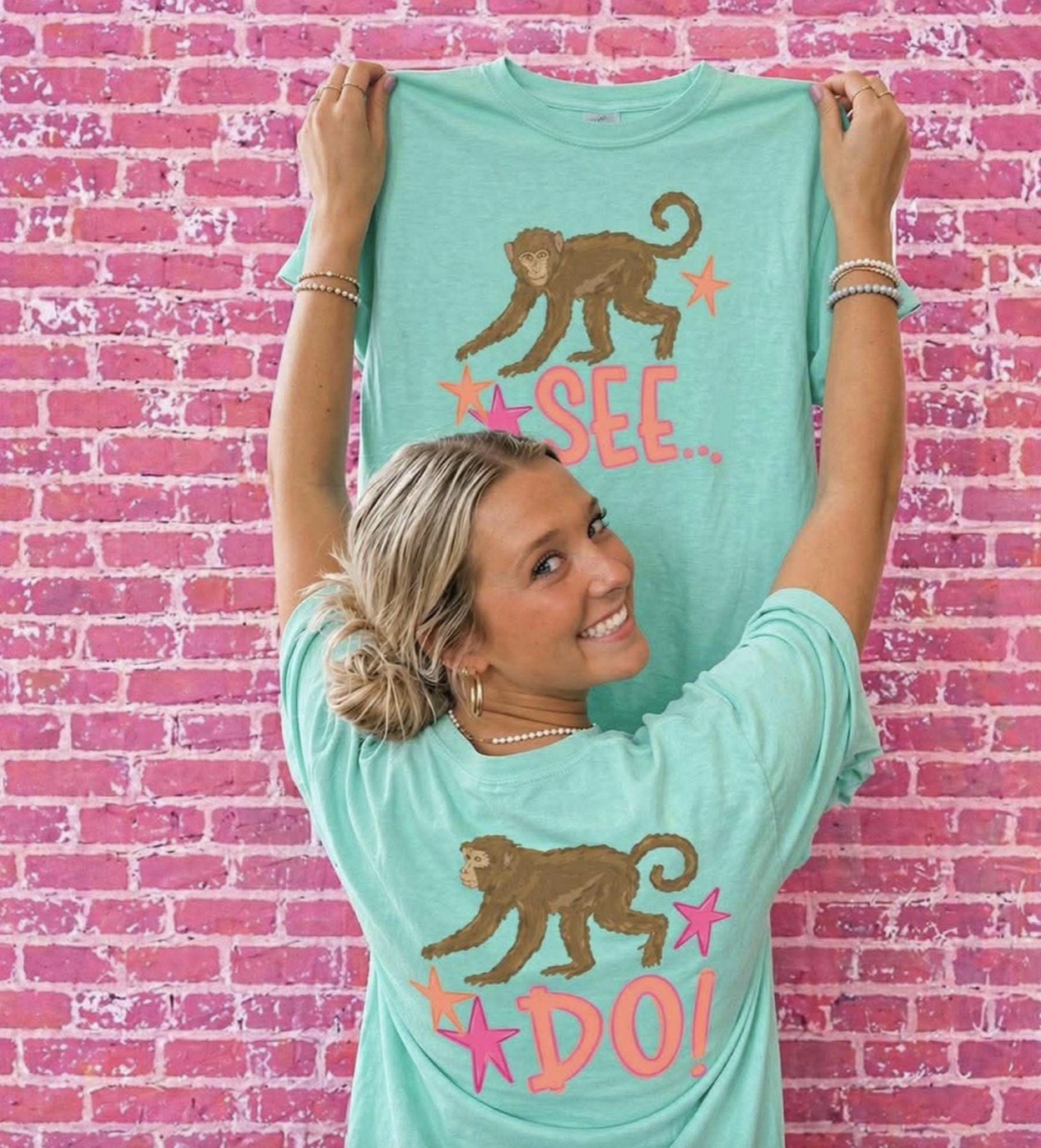 Woman modeling Island Reef Comfort Colors Monkey See Monkey Do graphic t-shirt set with front and back design against pink brick wall