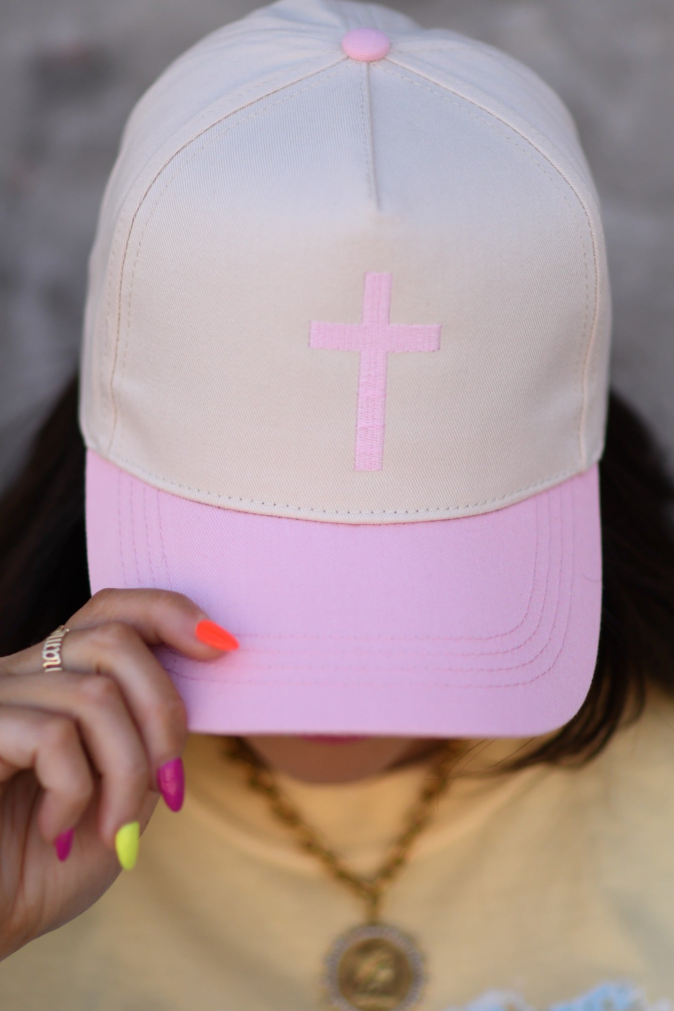 Woman wearing butter yellow church graphic tee with pastel design and pink cross embroidered snapback hat