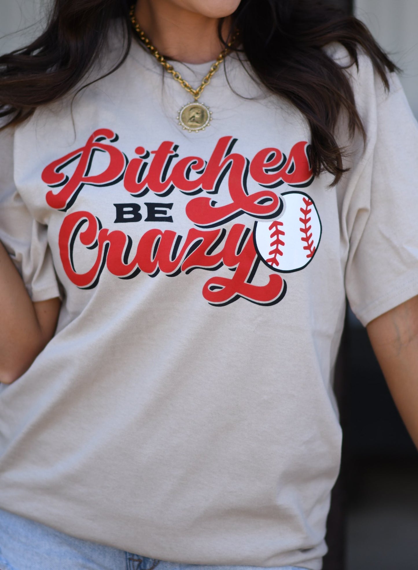 Woman wearing beige “Pitches Be Crazy” baseball graphic tee with red lettering and baseball design