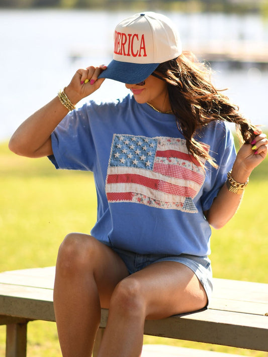 Woman wearing a vintage quilted American flag graphic t-shirt in Flo Blue Comfort Colors, styled with denim shorts and patriotic accessories outdoors