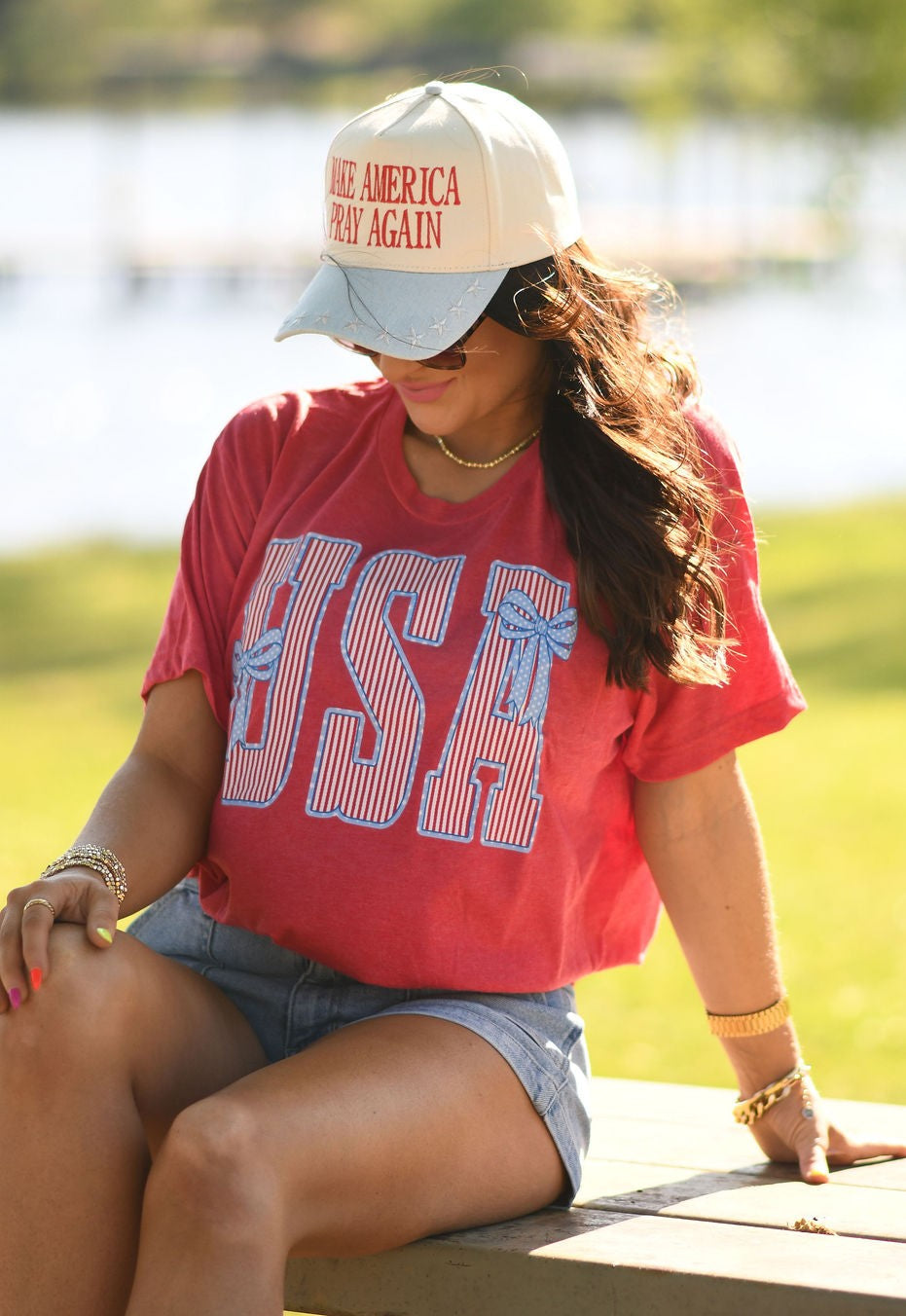 Woman wearing heather red USA patriotic bow graphic t-shirt styled with denim shorts outdoors in summer