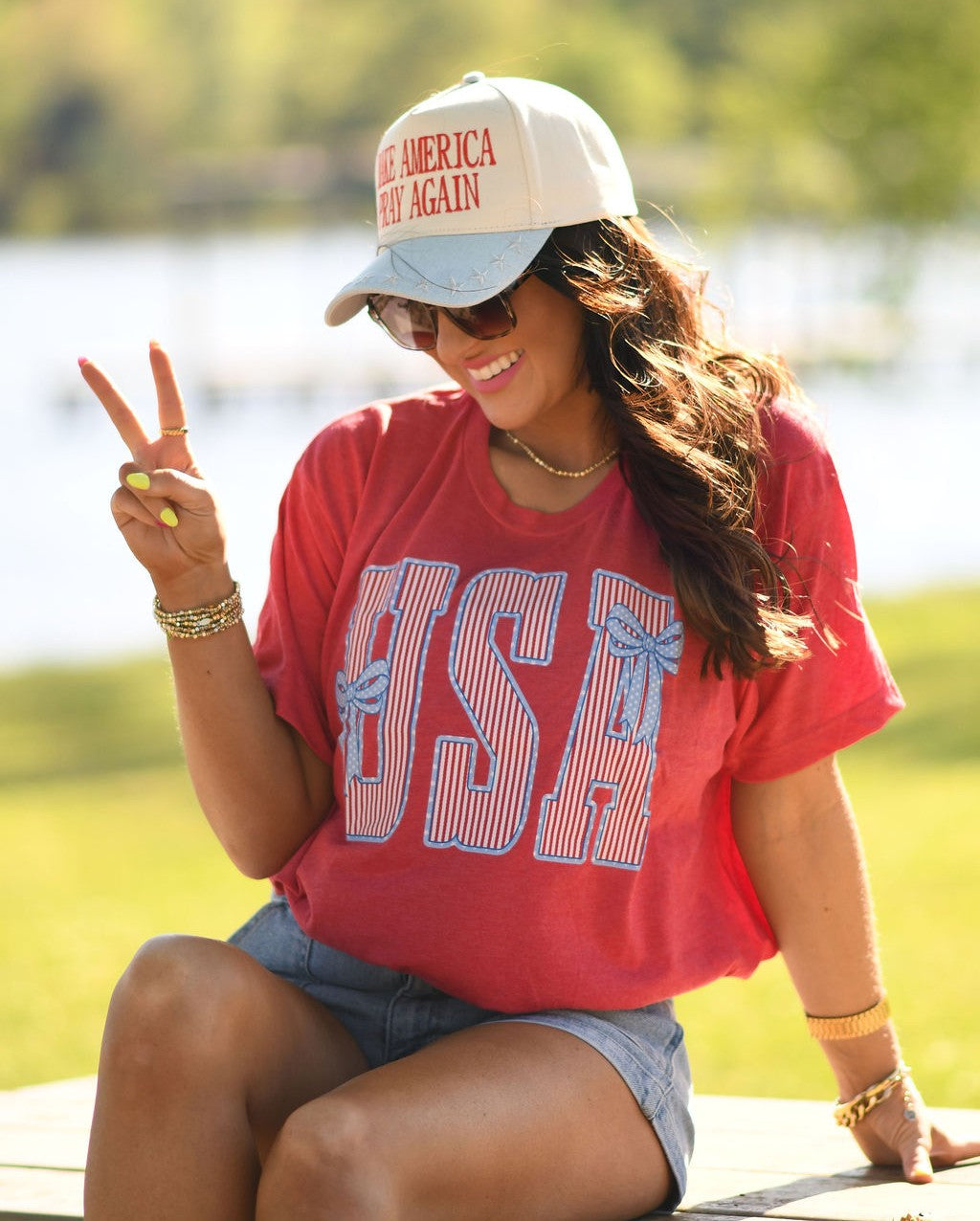 Woman wearing heather red USA patriotic bow graphic t-shirt styled with denim shorts outdoors in summer