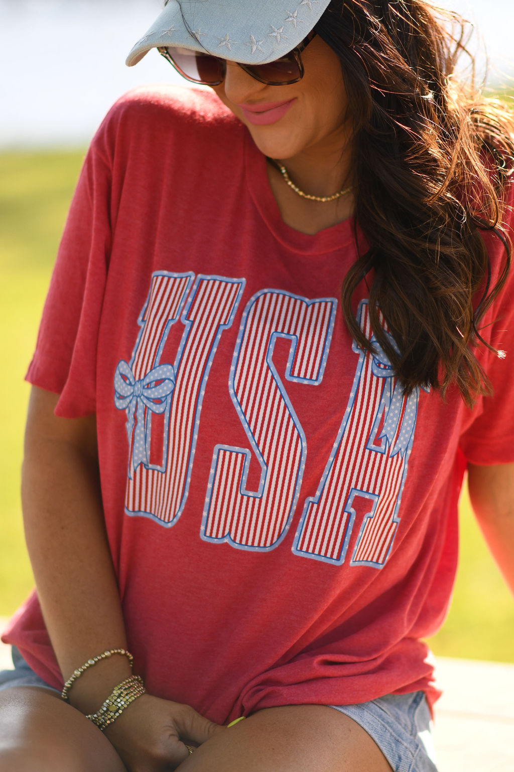 Woman wearing heather red USA patriotic bow graphic t-shirt styled with denim shorts outdoors in summer