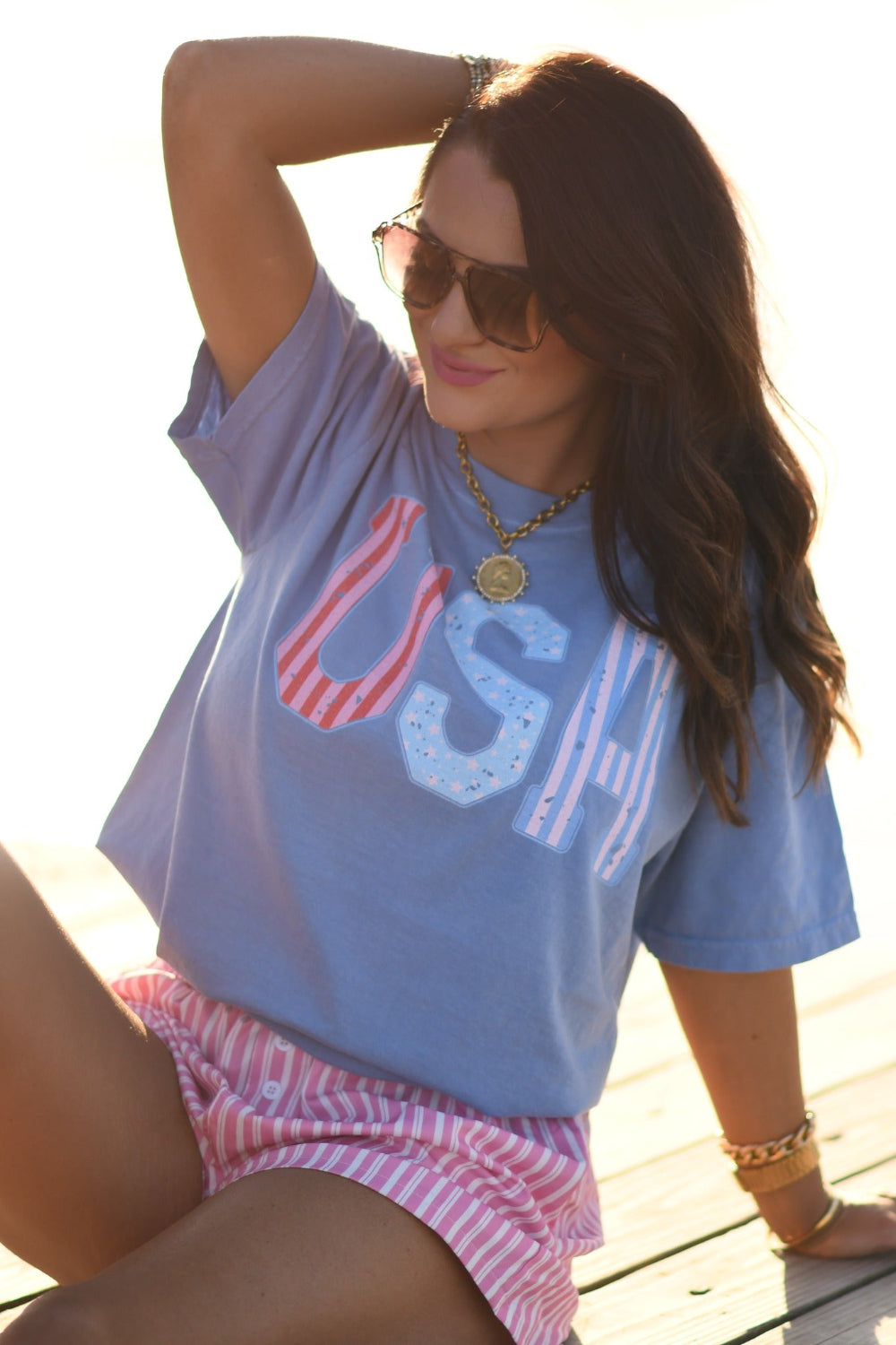 Woman wearing washed denim Comfort Colors USA stripes patriotic graphic tee with pink striped shorts