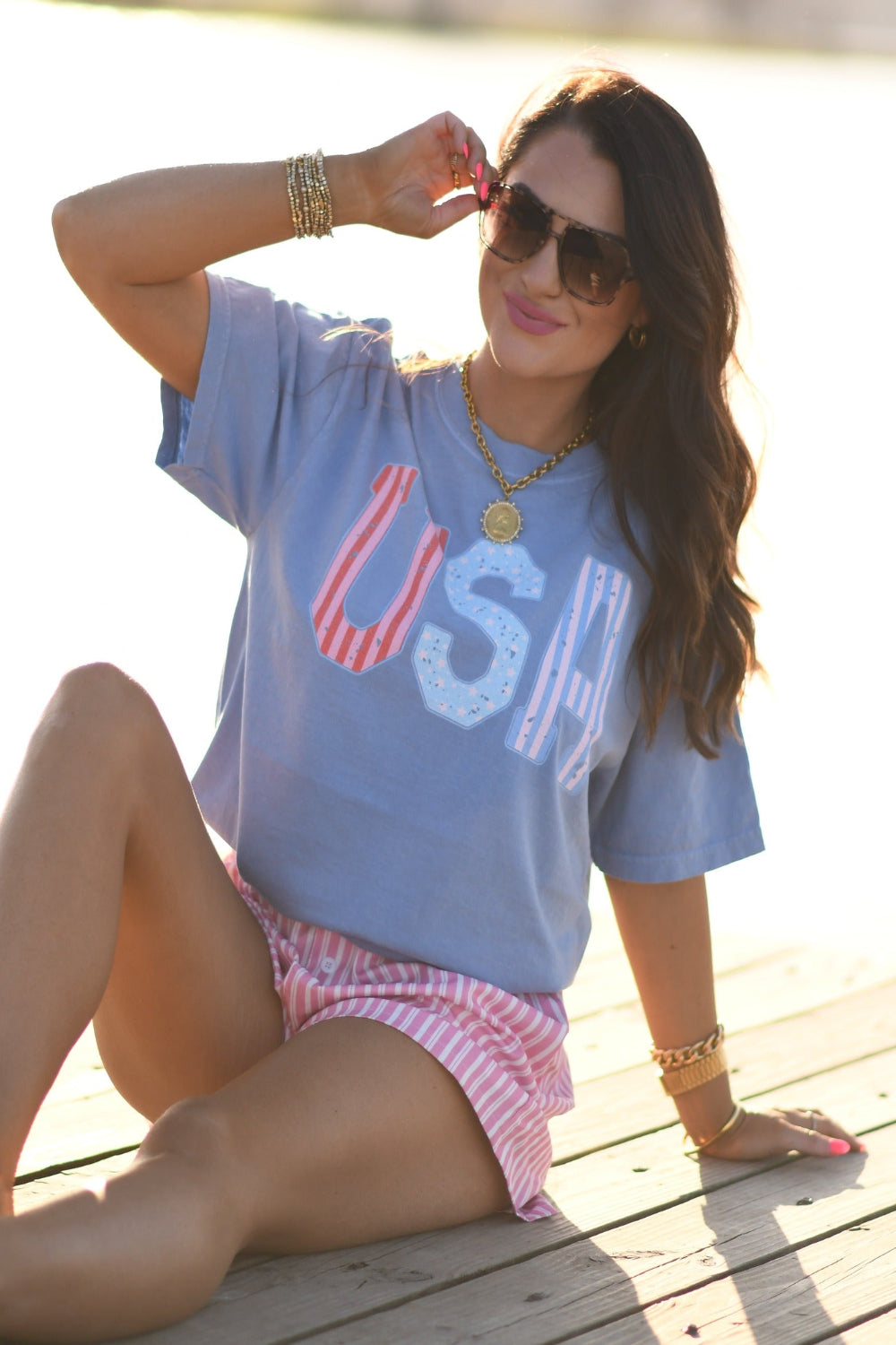 Woman wearing washed denim Comfort Colors USA stripes patriotic graphic tee with pink striped shorts