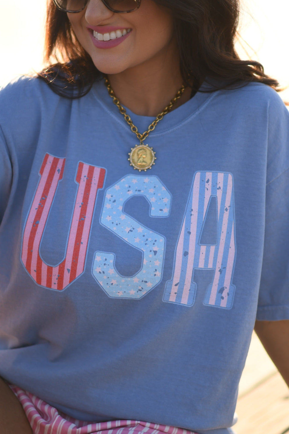 Woman wearing washed denim Comfort Colors USA stripes patriotic graphic tee with pink striped shorts